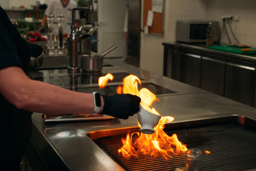 The flames in the kitchen of the restaurant. The chef prepares a steak in the restaurant's kitchen.