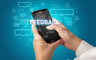 Female hand typing on smartphone with FEEDBACK inscription, social media concept