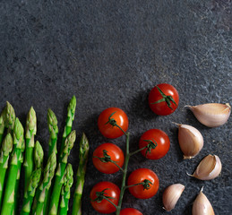 fresh asparagus, tomatoes and garlic on a dark background. Ingredients for cooking. Place for recipe or textm