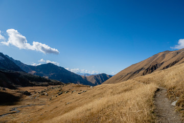 Fototapeta na wymiar Juta trekking path landscape with river and mountains in sunny autumn day - popular trekking in the Caucasus mountains, Kazbegi region, Georgia.