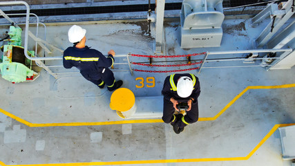 Two seaman on deck of container ship wearing boiler suit and helmets.