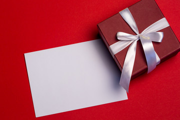 Blank paper and giftbox on red background, top view, Valentine's greetings card, copy space
