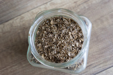 Dill seeds in a glass jar on a wooden background