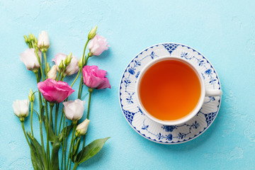 Cup of tea with pink flowers eustoma on blue background. Top view.