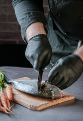 cleaning a fish with a knife on a wooden surface. hands in black gloves