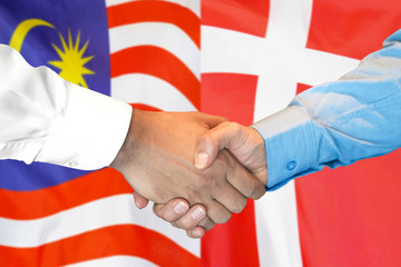 Handshake on Malaysia and Denmark flag background.