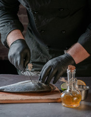 cleaning a fish with a knife on a wooden surface. hands in black gloves