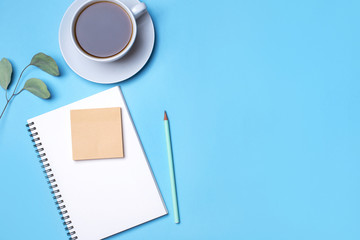 Blue background with notepad, pencil and cup of coffee. Top view with copy space, flat lay.