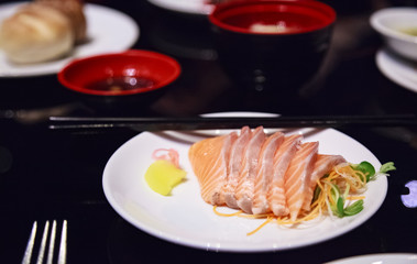 Selective Focused Japanese salmon sashimi (fresh fatty salmon meat) decorated with grated turnip and carrot in white dish on marble table background. Nutrition, Traditional Oriental Asian Food concept