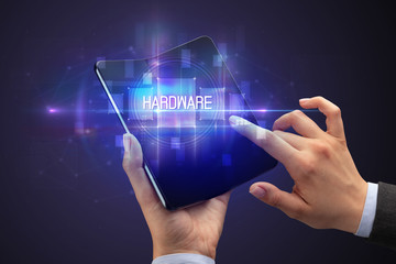 Businessman holding a foldable smartphone with HARDWARE inscription, new technology concept