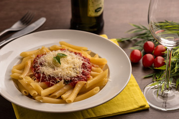 Penne pasta in bolognese sauce in white dish on yellow cloth on wooden table