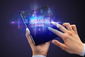 Obraz premium Businessman holding a foldable smartphone with APPLICATION inscription, new technology concept