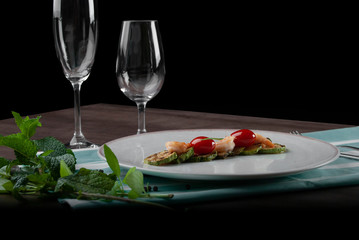 Shrimps, zucchinis and cherry tomatoes in white plate above the striped table game set with cutlery and glasses