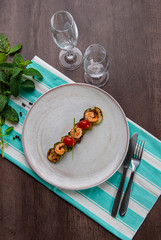 Shrimps, zucchinis and cherry tomatoes in white plate above the striped table game set with cutlery and glasses