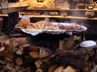 Pork ribs, sausages and potatoes in a large plate cooking on the street at the stake with firewood. Street food for tourists at the christmas market in Europe, medieval style food.
