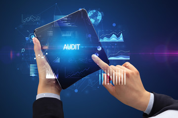 Businessman holding a foldable smartphone with AUDIT inscription, successful business concept
