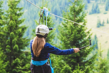 A young girl takes a picture of herself on a cellphone while descending on a zipline_