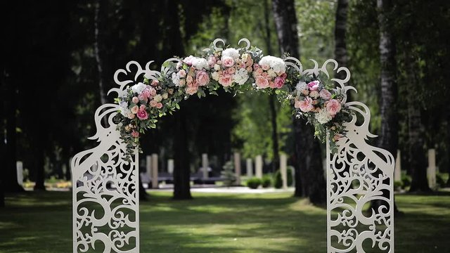 Wedding ceremony in white colors. Decorated arch with fresh flowers of roses, peons, chrysanthemums and green eucalyptus. Outdoor holiday