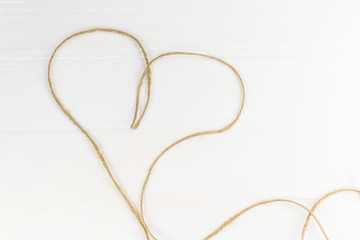 gray rope lies in the shape of a heart. Wooden background in white