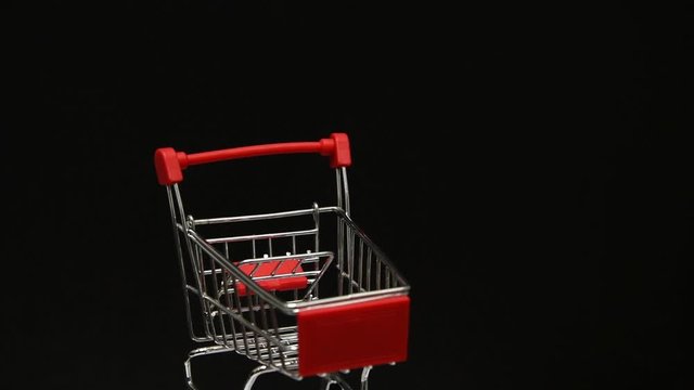 Rotating miniature metal empty shopping cart on black background. Shopping, sales theme