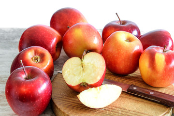 Fresh red apples whole and slices on the wooden kitchen board and on the rustic table. Healthy dieting food.