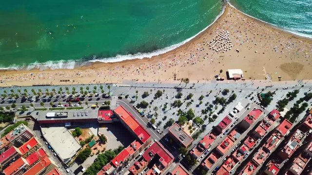 Aerial, reverse, drone shot, tilting over people on the Barceloneta beach, a road and buildings, in Barcelona city, on a sunny, summer day, in Catalonia, Spain