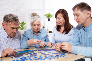 elderly couple and middle-aged couple working on a jigsaw puzzle together at home