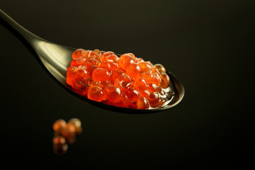 Nice black spoon with red caviar on the black background.healthy food concept.