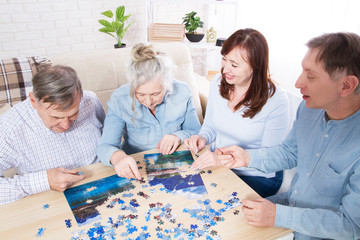 family play in puzzles at home, elderly couple and middle-aged couple working on a jigsaw puzzle together at home