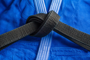 Black judo belt tied in a knot layng on blue judogi
