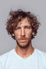 Freestyle. Man with curly hair in t-shirt standing isolated on grey serious close-up