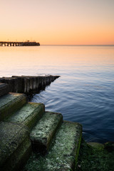 Stunning long exposure landscape image of orange sky over deep blue sea with steps in foreground