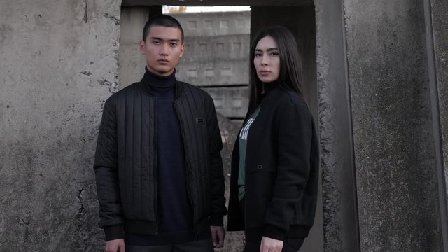 calm man with attractive girlfriend stands near grey concrete walls at abandoned construction site slow motion