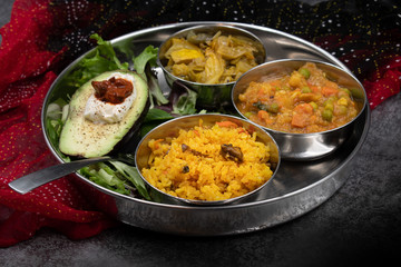 Indian food platter with serving bowls: mixed veggetable curry, cabbage curry, rice pilaf, salad and avocado