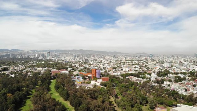 Drone flying backwards over Centro Nacional de las Artes and a Golf Course in Mexico City with a blue sky as background