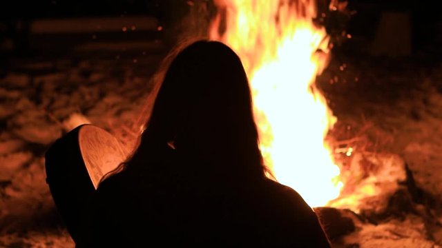 A native warrior man is seen from behind after a successful buffalo hunt, burning a fire in nature by night, playing a sacred drum to worship gods