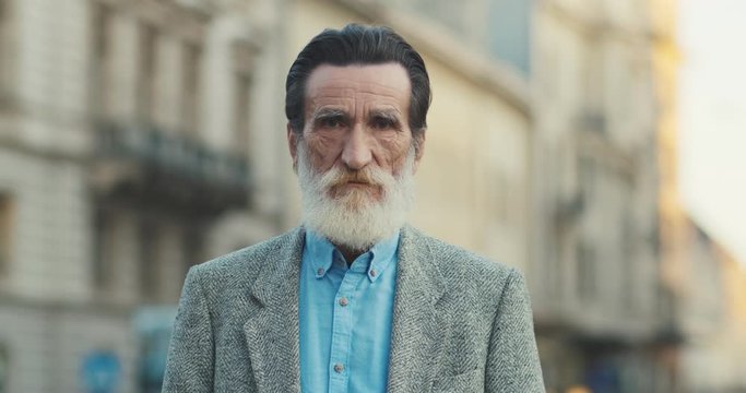 Portrait of the good looking old Caucasian grandfather, olf man with a long grey beard looking straight to the camera. Close up. Outside.