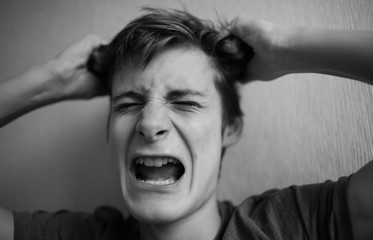 Teen guy squeezes his head and screams and grimaces on a light background