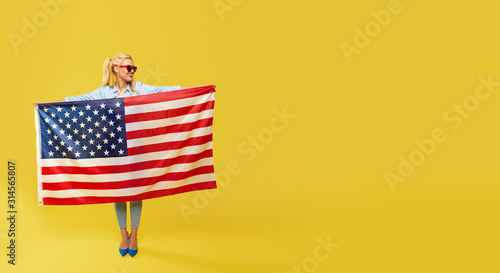 American girl. Happy young woman in denim clothes holding USA flag isolated on yellow background. Banner. Copy space for text