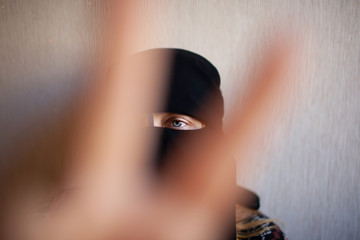 A woman in Muslim clothes shows her victory sign with her fingers out of focus on a light background