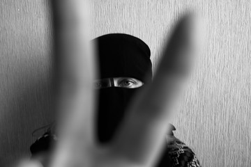 A woman in Muslim clothes shows her victory sign with her fingers out of focus on a light background