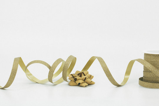 Bobine de bolduc dor&eacute; &agrave; paillettes d&eacute;roul&eacute;e pour faire les cadeaux de no&euml;l ou pour anniversaire avec n&oelig;ud en bolduc photo studio sur fond blanc avec espace texte