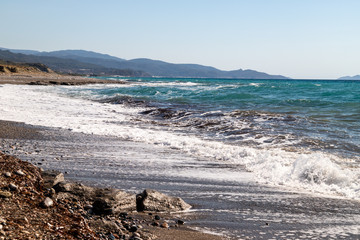 Fototapeta na wymiar View at the coastline with pebble beach and water waves on the westside of Greek island Rhodes