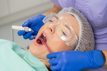 Naklejka premium Close-up of a girl’s patient at the moment when the dentist is using a saliva ejector to clean the oral cavity during the process of calculus removal.
