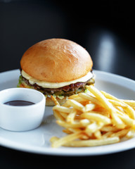 Appetizing juicy burger with french fries and sauce on a white plate