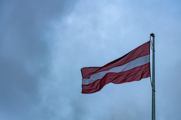 State flag of the Republic of Latvia against a stormy sky.