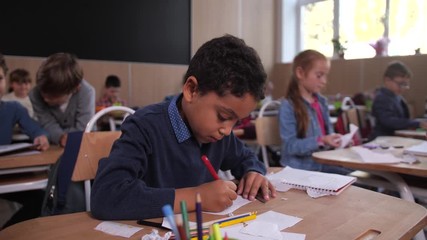 Cute preadolescent schoolboy drawing with concentration during art lesson in elementary school. Focused mixed race primary school student enthusiastically creating picture in drawing lesson