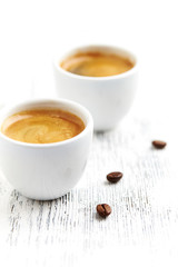 Two cups of coffee on bright wooden background.