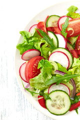Healthy salad with tomatoes, cucumber, radish, lettuce and rocket. Bright background. Close up.