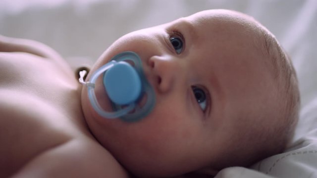 Caucasian baby looks into camera, then looks up while sucking on pacifier